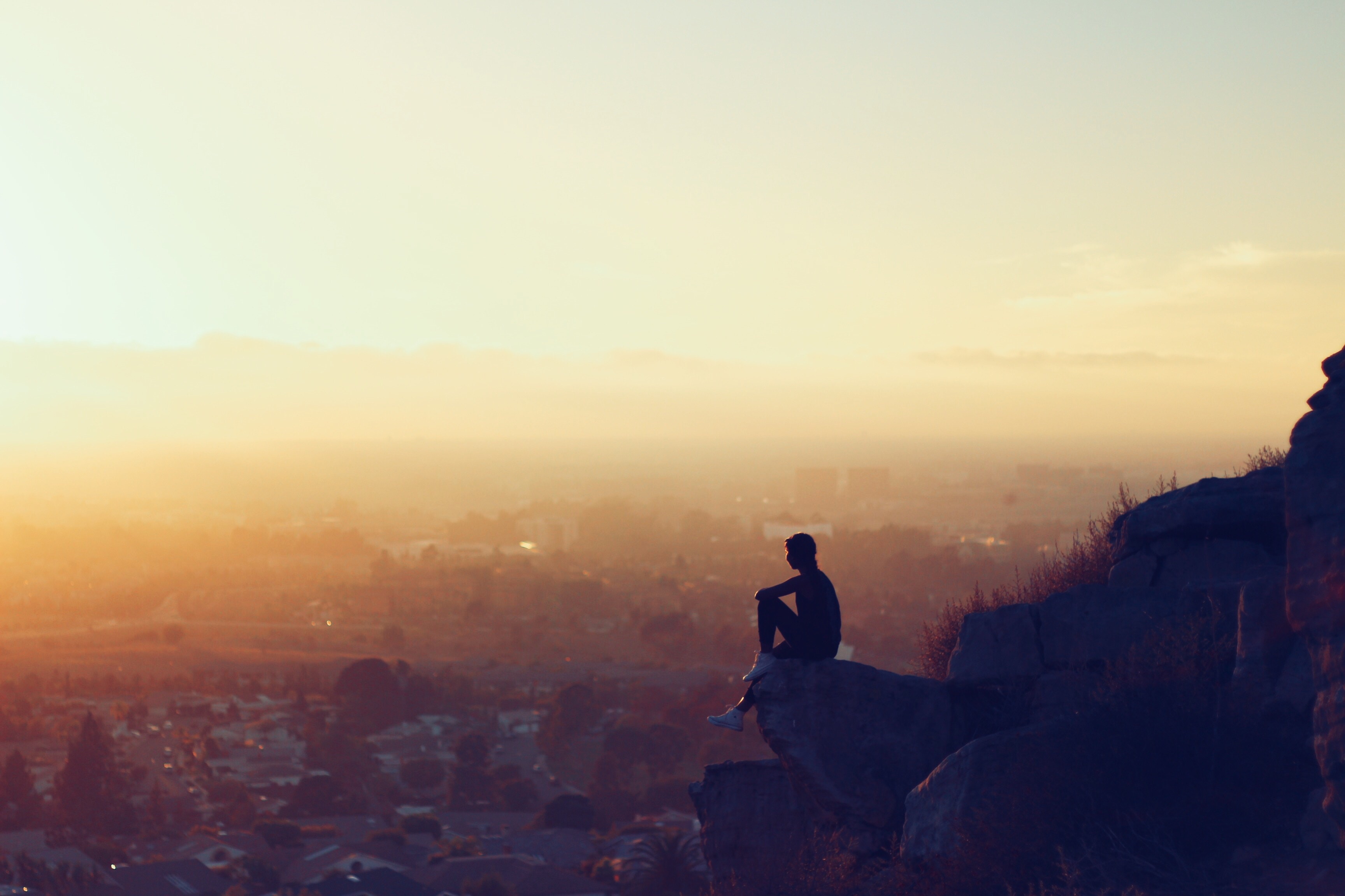 A Man Sitting On A Rock Formation Cliff During Golden Hour