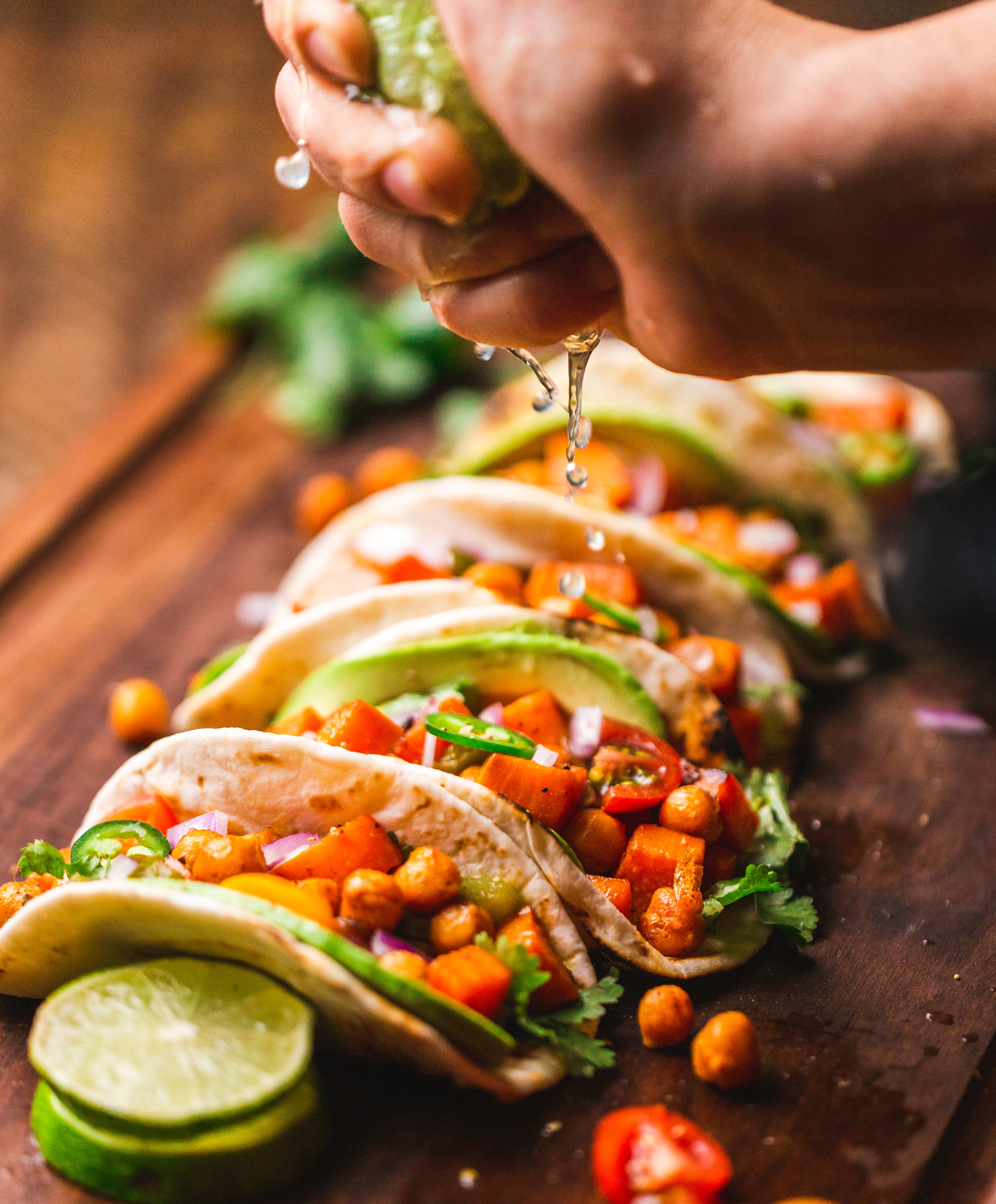 A Hand Squeezing Lime Juice Over A Line Of Tacos Filled With Avocado And Peppers