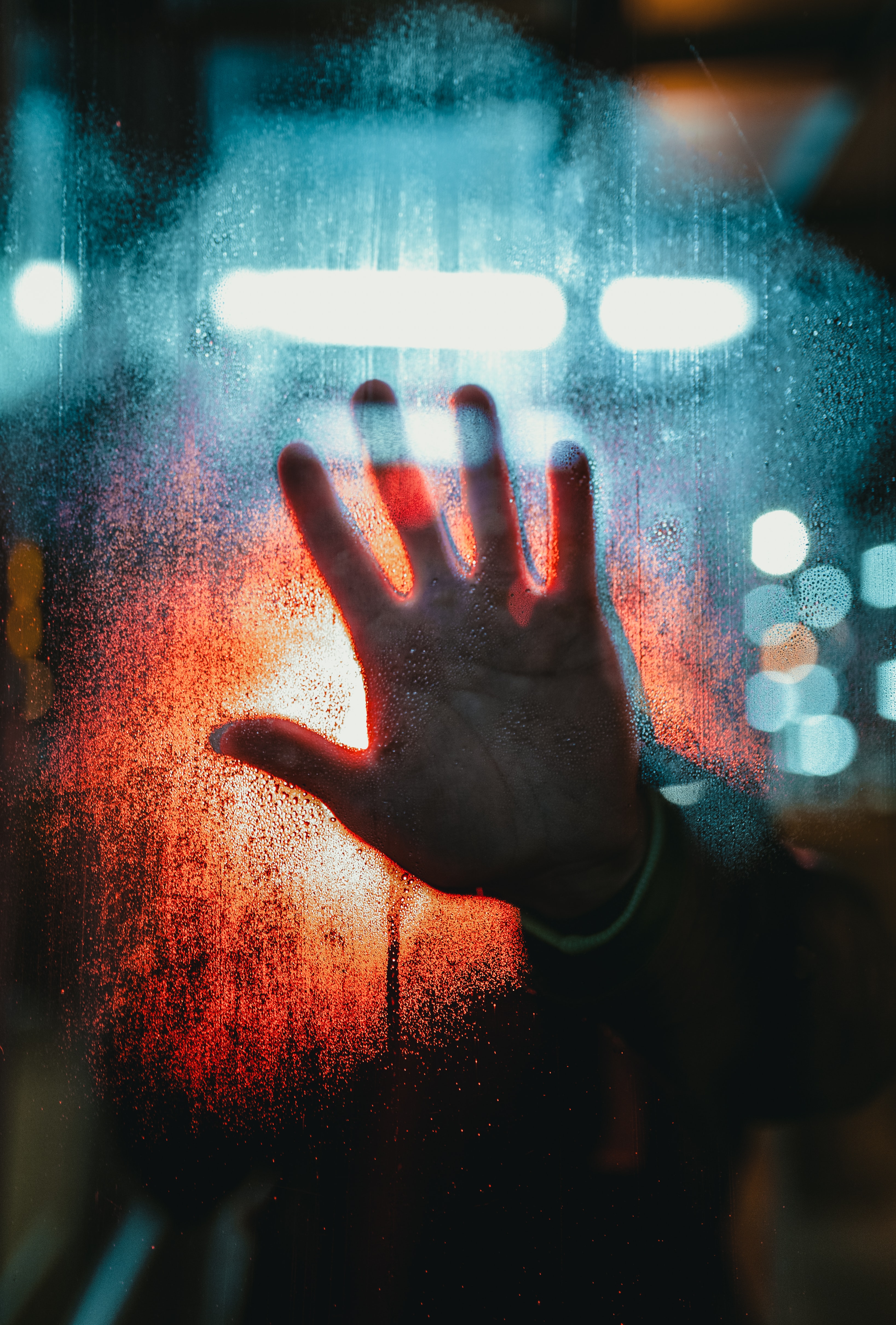 A Hand On Wet Glass, With Blue And Red Lights In The Background