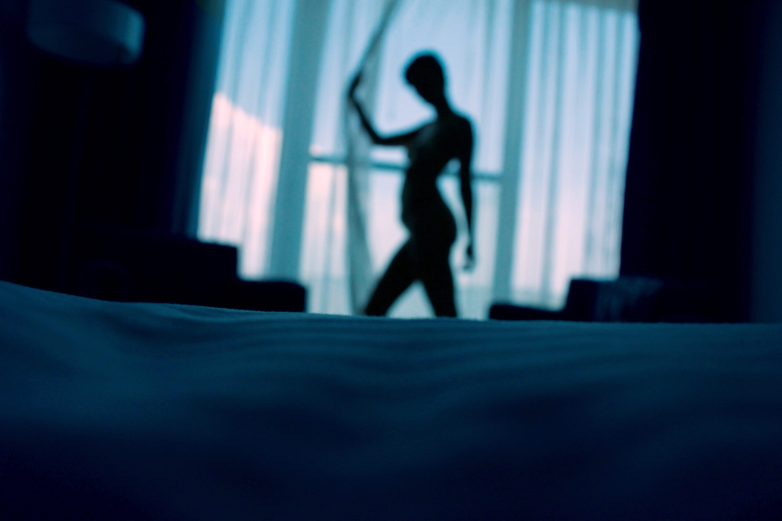 Silhouette Of Woman In A Dark Bedroom Opening Up A Window Curtain