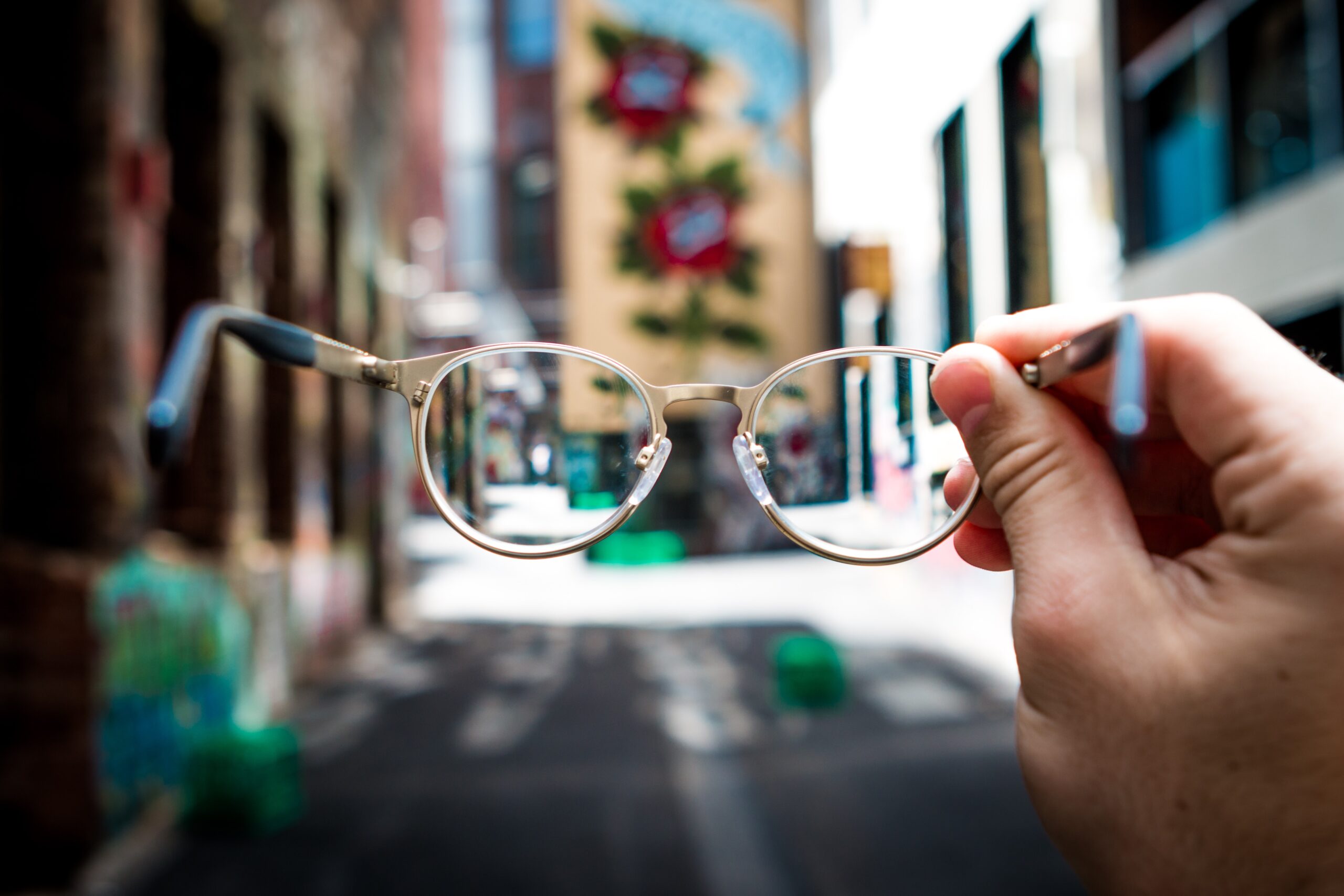 Image Of Hand Holding Eyeglasses Against Blurred Backdrop