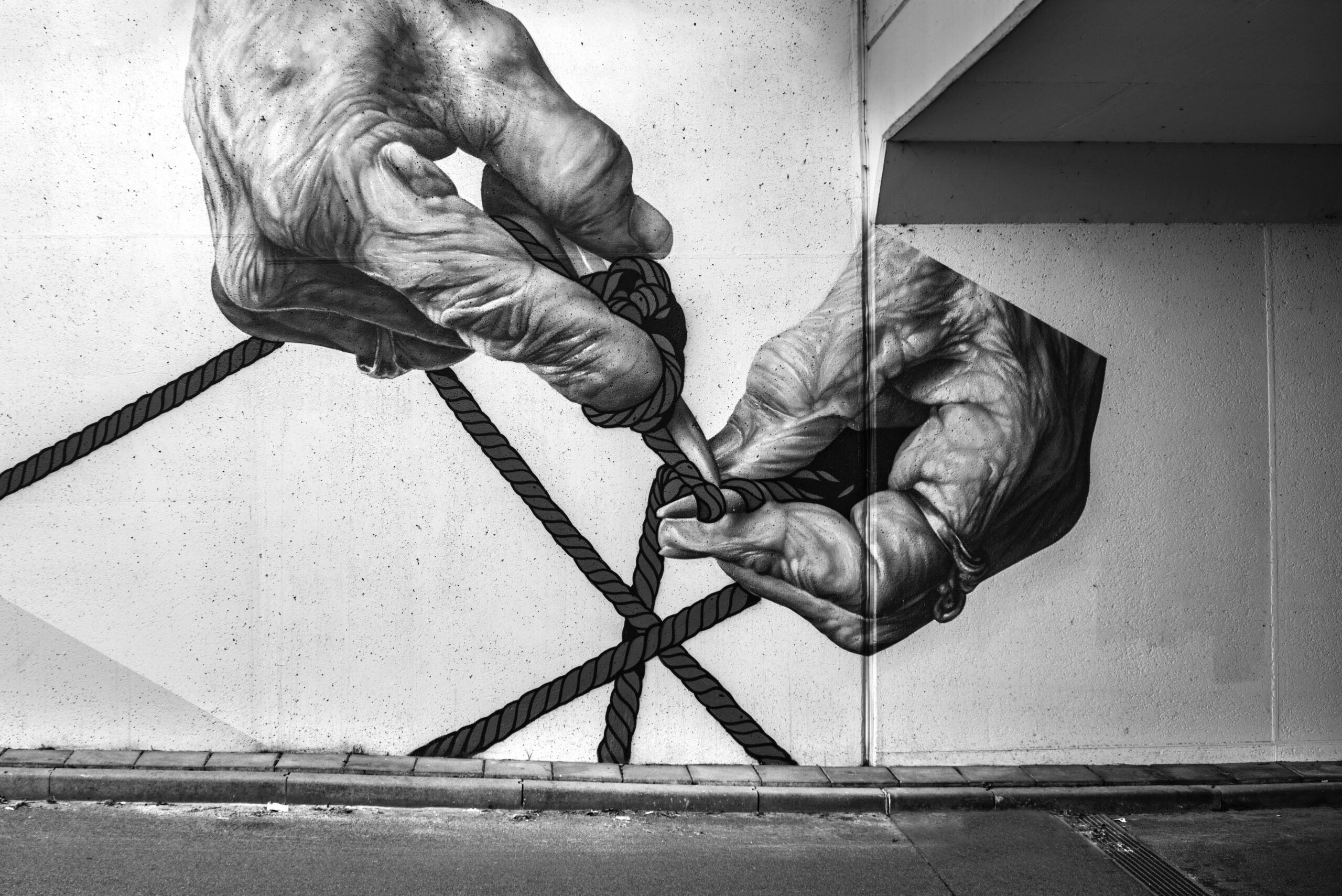 Image Of A Mural In Black And White That Features Two Hands Knitting. The Hands Are Wrinkled And So Are Likely From An Elderly Person