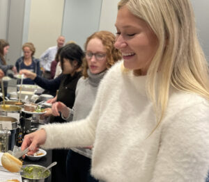 A row of young women help themselves to serving dishes of plant-based meals.