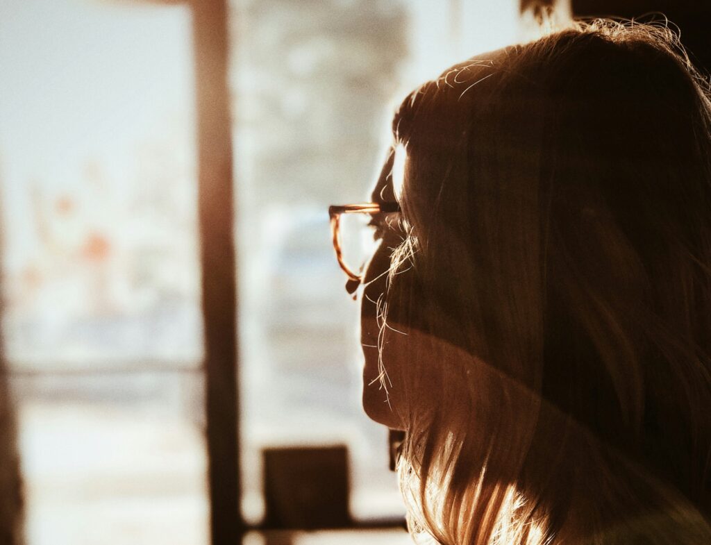 Seen from behind, a woman gazes through a shop window into the street.