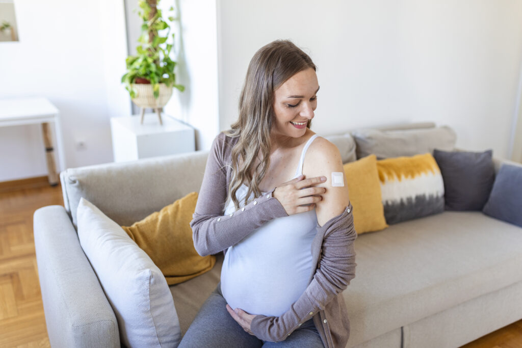 Pregnant woman with adhesive bandage on her arm after vaccine.